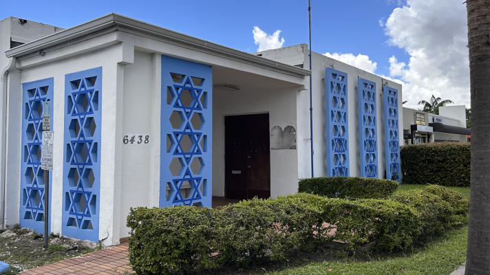 A white building decorated with blue stars of david at the entryways. A shadow is by the front door where a plaque once was.