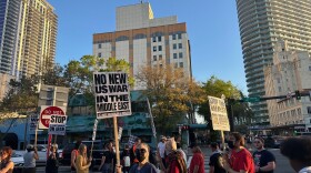 people holding protest signs, some wearing masks, gathered on the intersection of 3rd street and first avenue of downtown St. Petersburg
