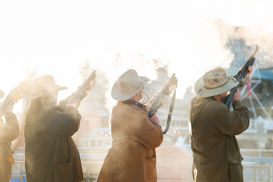 Three men in Rough Riders hats and coats firing rifles into the air