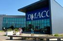 A woman wearing a backpack walks out of a large building with the words "DMACC" and "student center." She is accompanied by a toddler girl and an older boy. Two other figures can be seen in the background. People leave the Student Center building on Monday, July 28, 2025, at the Ankeny campus of Des Moines Area Community College in Ankeny, Iowa.