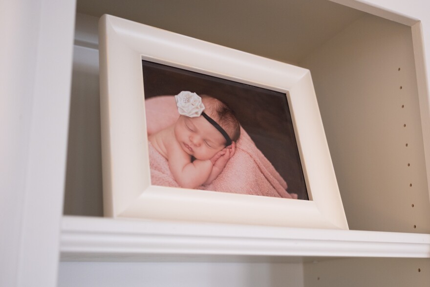 A close-up of a photograph of Marley Mansour as a baby in a white frame on a white bookshelf.
