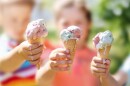 3 children blurred in background each holding up an ice cream cone of different flavors with ice cream melting down the side of the cone