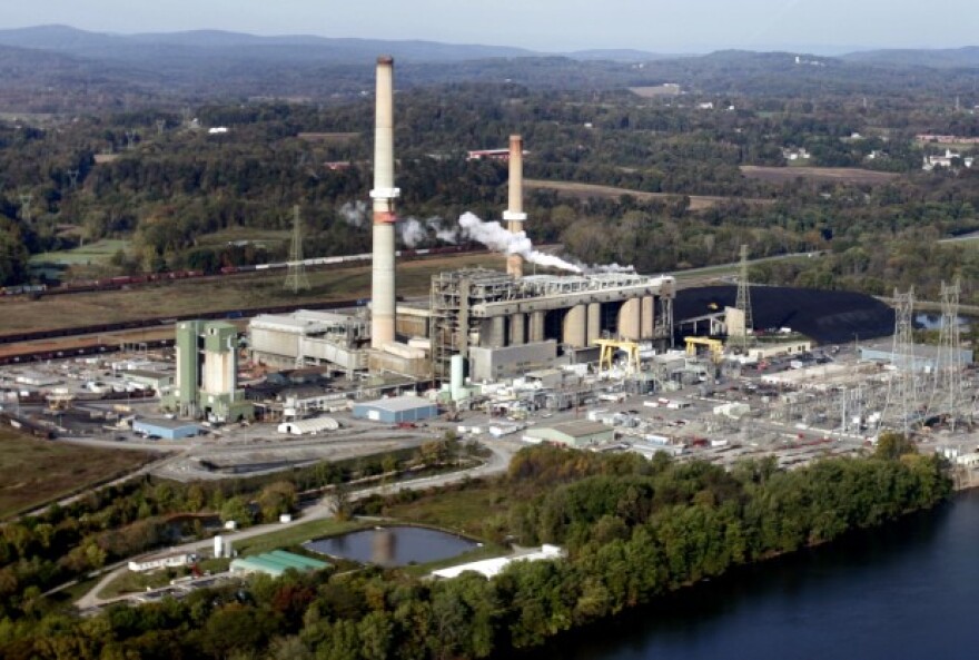 Smoke rises from a coal-fired power plant next to a river in a rural area.