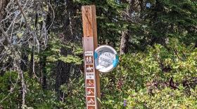 A small paper plate with the words "trail magic, July 12-14" is attached to another sign listing what methods of transport are allowed on the trail. There's an arrow on the paper plate pointing to the left.