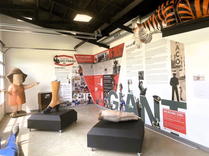  Oversized figurines, including a woman's foot and a pale hand, sit on pedestals. Behind time is a large historical timeline printed on white walls.