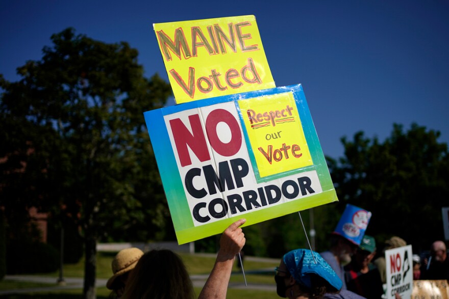 A protester holds a sign outside the Augusta Civic Center where a state meeting on Central Maine Power's proposed hydropower corridor is taking place, Wednesday, July 20, 2022, in Augusta, Maine.