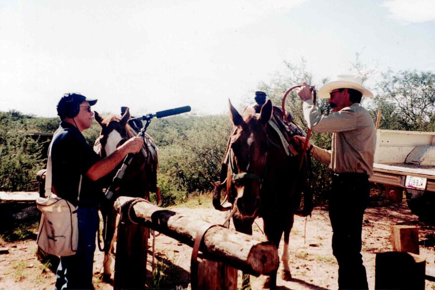 Man with microphone talking to cowboy poet and horse. 