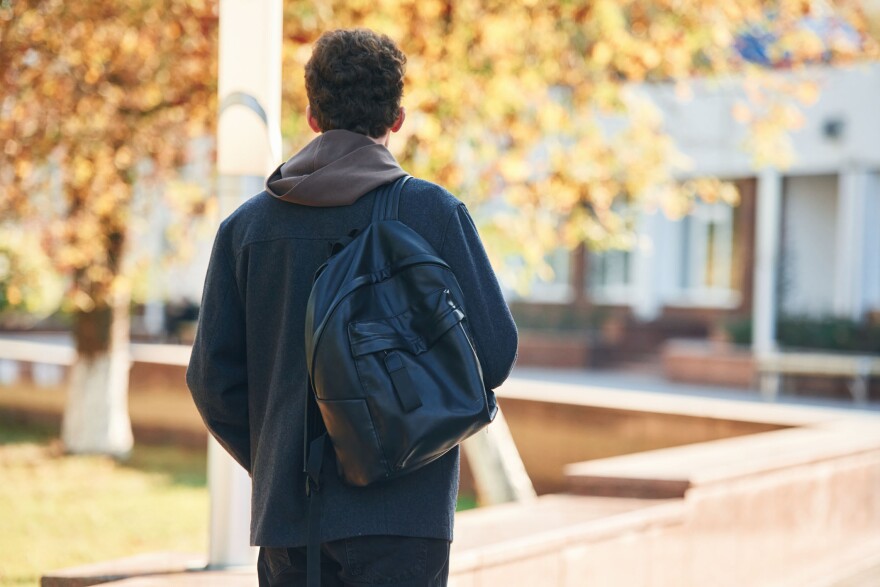 Back view. Young student is outside the university, in black clothes.