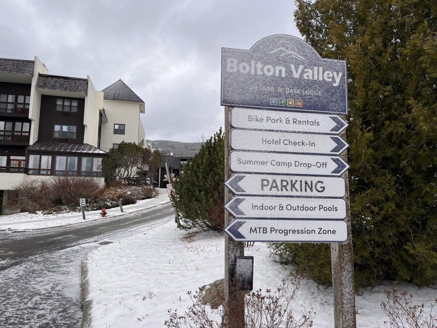 A series of signs with snow caked on reads "Bolton Valley" and points toward parking, rental check-ins, pools and more.