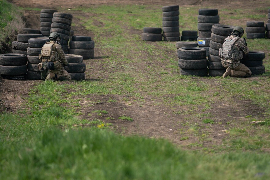 A Ukrainian reconnaissance team hides behind stacks of tires in an exercise.