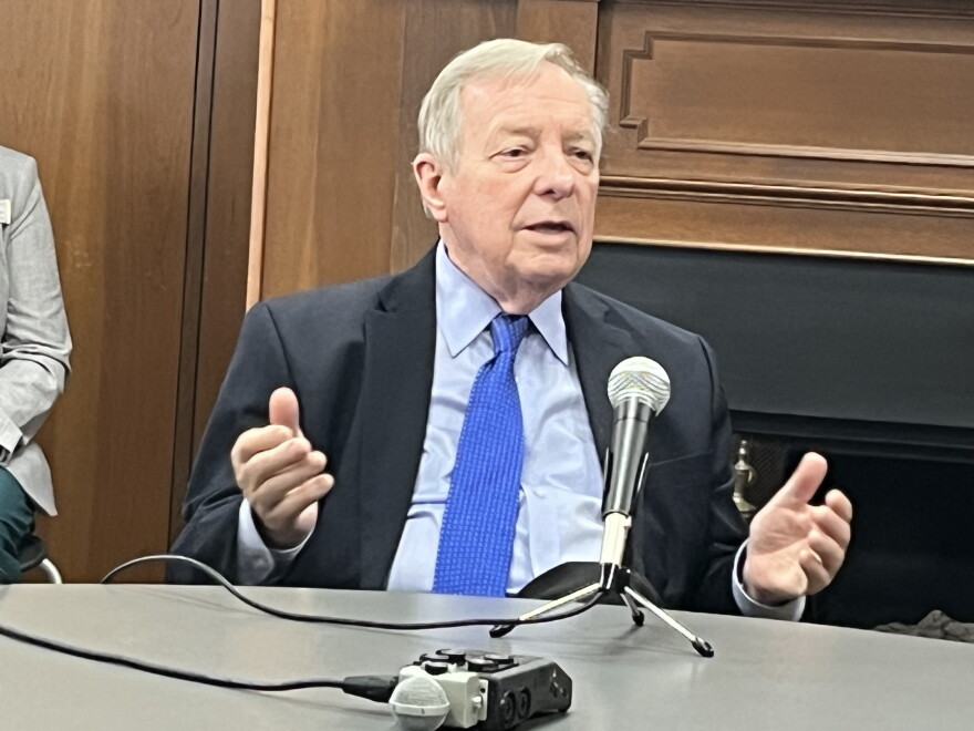 U.S. Senator Dick Durbin sitting at a round table with a microphone on it. His shirt is light blue. His tie is vibrant cerulean. 