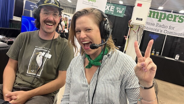A man smiles and a smiling woman gives the peace sign to the camera
