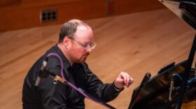 A person seated at a piano with one hand held partly up