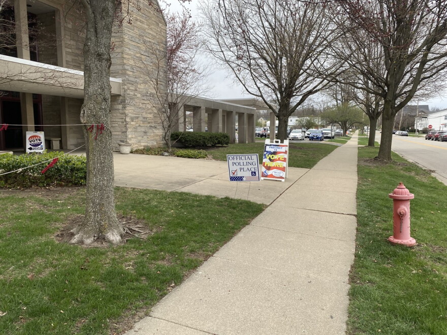 Sidewalk entrance to a church that includes a sign with wording 'Official Polling Place' and a sandwich board with an image of an American flag and the words 'Vote Here' on the side. 