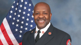 Clayton Farr poses in a suit, holding his fire chief cap on his side.
