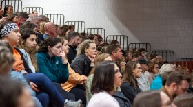 A packed crowd of onlookers show many tense facial expressions as they listen to a presentation.