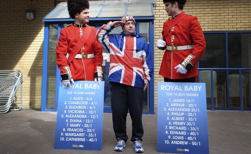 Royal supporter John Loughrey salutes as men dressed as soldiers carry boards with proposed baby names Friday outside the Lindo Wing of St. Mary's Hospital in London.