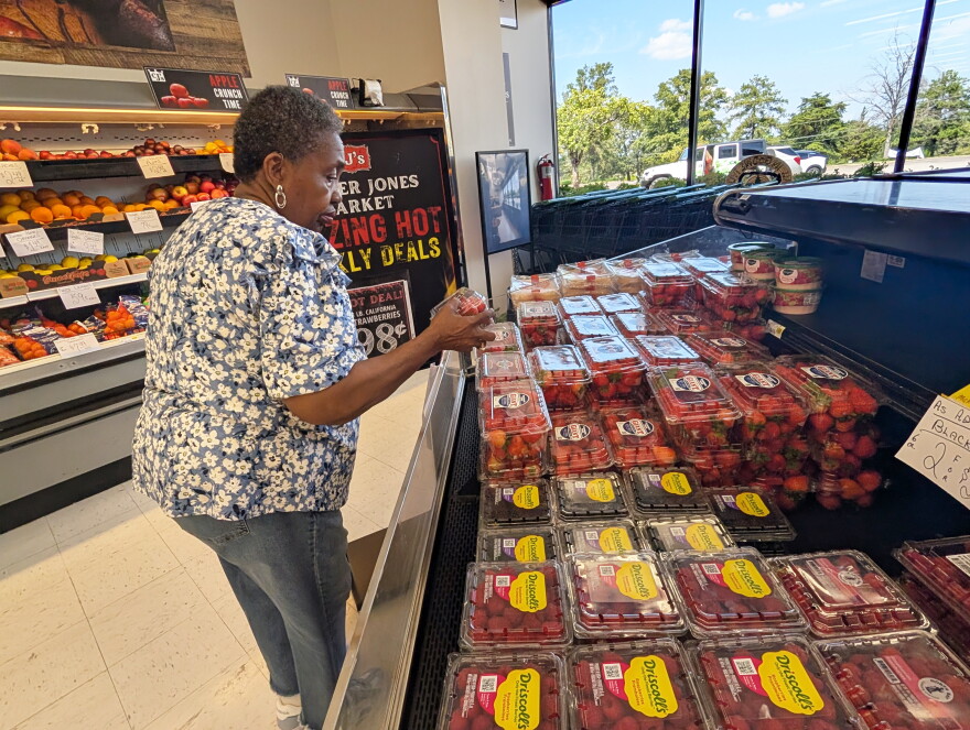 A women picks up a package of fresh strawberries and examines it.