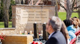 Ceremony attendees sit in a row of chairs alongside the Redbird Remembrance memorial on the Illinois State University campus listing the names of the seven men who died in a 2015 plane crash: Aaron Leetch, Torrey Ward, Scott Bittner, Jason Jones, Andrew Butler, Terry Stralow and Thomas Hileman.