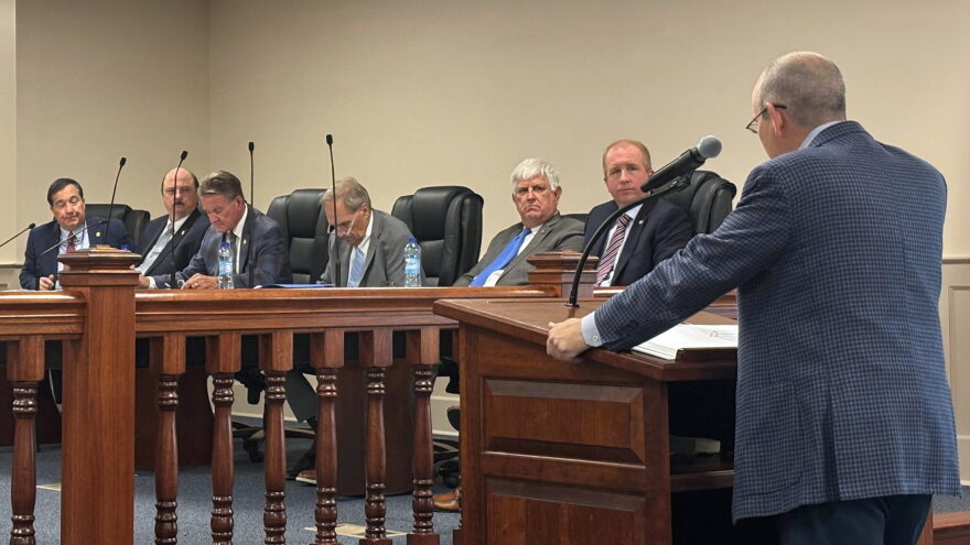 Alabama Senator Clyde Chambliss stands behind a podium and speaks to fellow lawmakers who sit behind a table.