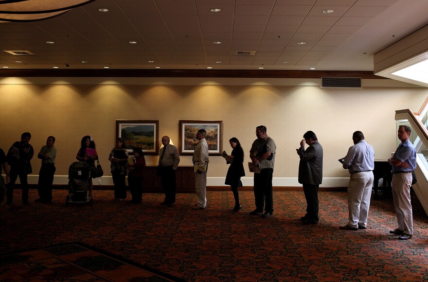 Job seekers read pamphlets as they wait in line to enter a job fair in San Jose, Calif.