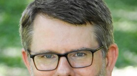 Bill Verble with a short gray beard, glasses, and a checkered blazer.