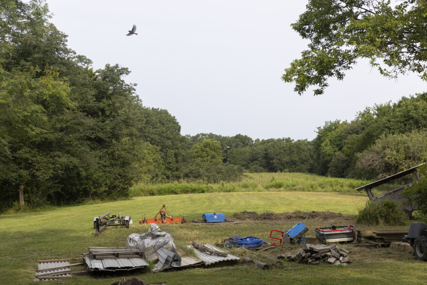 A bird flies over Dan Kuebler’s equipment from when he was a gardener on Aug. 13, 2026, in Ashland, Mo. When Kuebler sold his land in 2025, he arranged to still live at the cabin “until (he) died.”