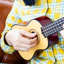 Asian pretty girl playing the wooden Ukulele in living room.