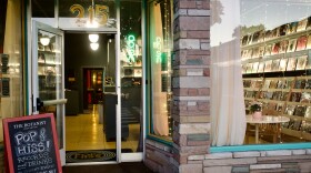 A sandwich board has a business named written in chalk next to an open door and glass windows that show a record shop. 