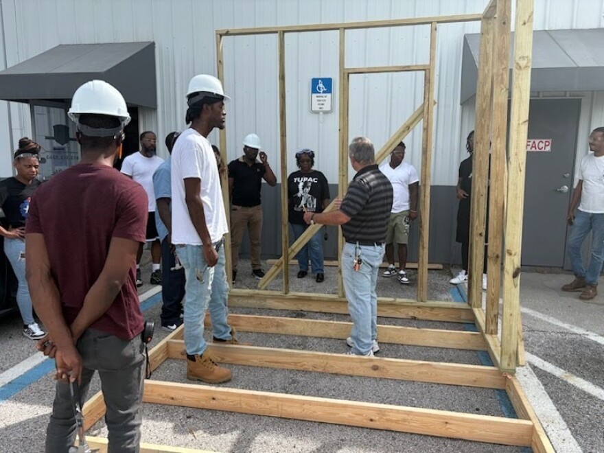 Vocational students with the CDC of Tampa wear hard hats and stand in a parking lot to learn wall framing during an intro-to-construction training for adults.