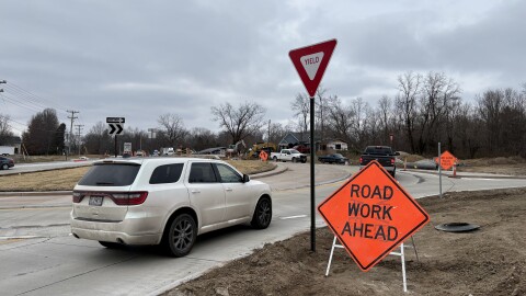 A white SUV drives through a newly constructed roundabout on the south side of Columbia. A orange sign on the right side reads "road work ahead."