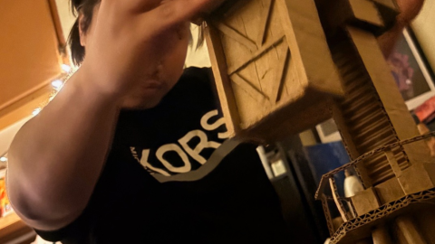 Jeimax Ruloma working on The Crane. Ruloma constructs industrial machines from fragile cardboard materials, exploring the precarious nature of capitalist systems and the tension between strength, labor, and impermanence.