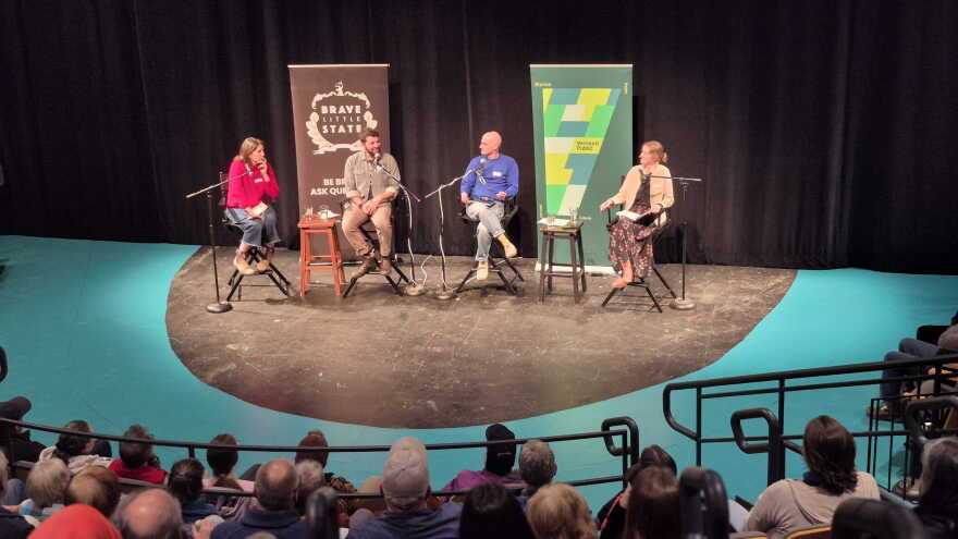 four people sit on chairs facing a seated audience
