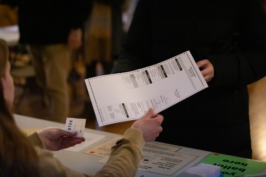 Poll worker Hannah Sorensen hands a ballot for the primary elections to a voter at the Gates of Heaven polling location in Madison, Wis., on Feb. 21, 2023.