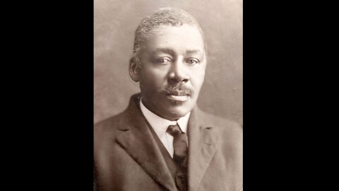 An old, grainy, black and white photo shows a man in a suit.