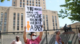 A protester rallies in front of Kansas City, Missouri, City Hall. She wears a pink t-shirt and holds a sign that reads, "You didn't like wearing a mask, imagine being told you have to have a baby." 