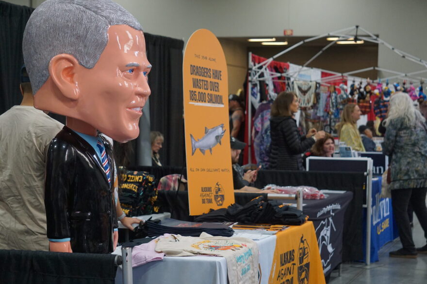 A plastic statue representing U.S. Sen. Dan Sullivan, R-Alaska, labeled "Yes Man Dan," stands on Oct. 23, 2026, at a booth manned by the liberal-leaning 907 Initiative at the Alaska Federation of Natives convention arts fair. The "Yes Man Dan" slogan is part of the group's criticism of Sullivan for his allegiance to President Donald Trump. The booth also features banners criticizing Sullivan on fishery management issues. Nearby is a booth promoting Sullivan's reelection and manned by the senator's wife, Julie Fate Sullivan.