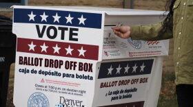 A voter drops off their ballot at a ballot drop box outside that has red white and blue coloring.