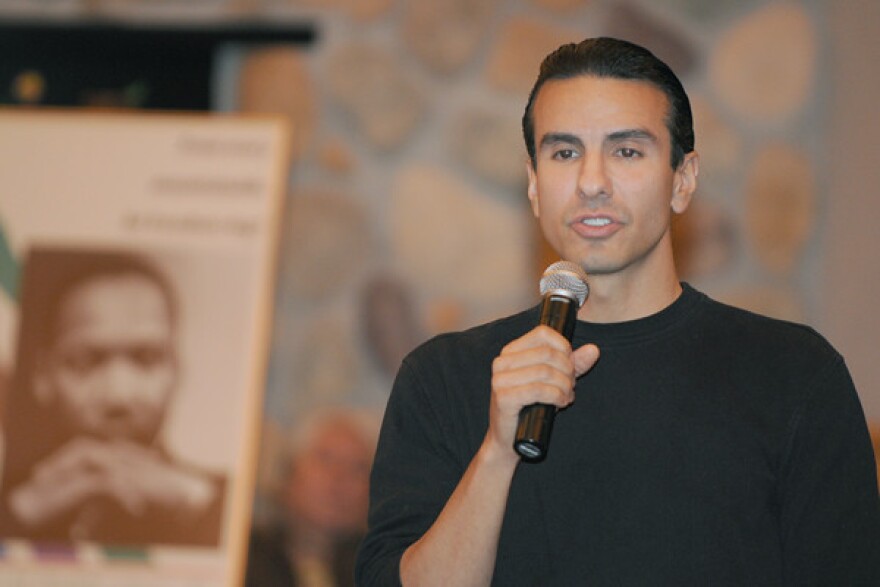 A man wearing black, holding and speaking into a microphone