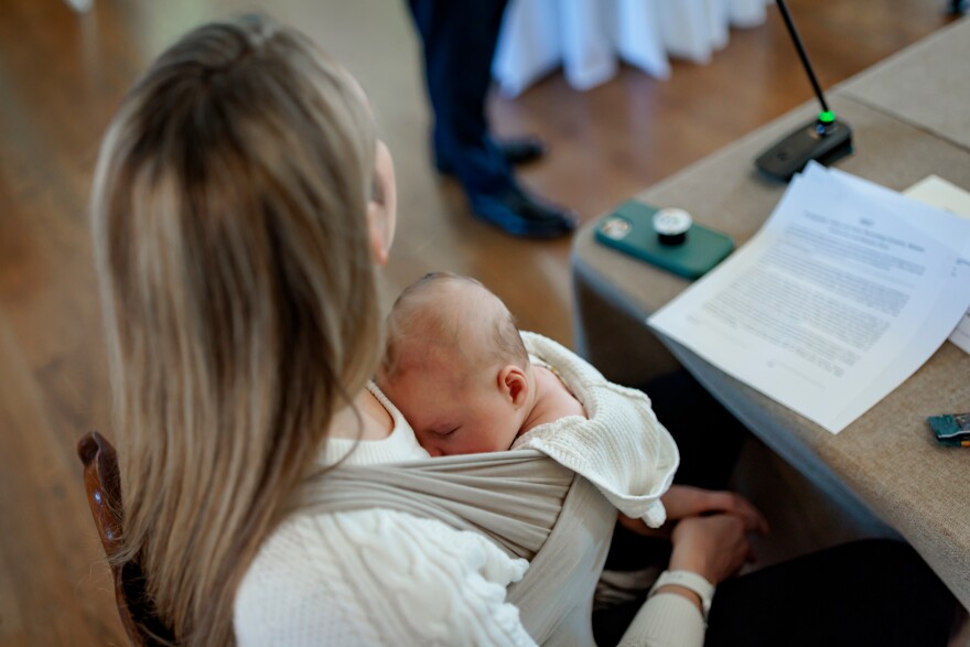 A woman sits while an infant rests on her chest.