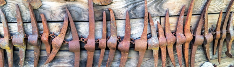 A row of rusty red pick axes sits against a dull wood background.