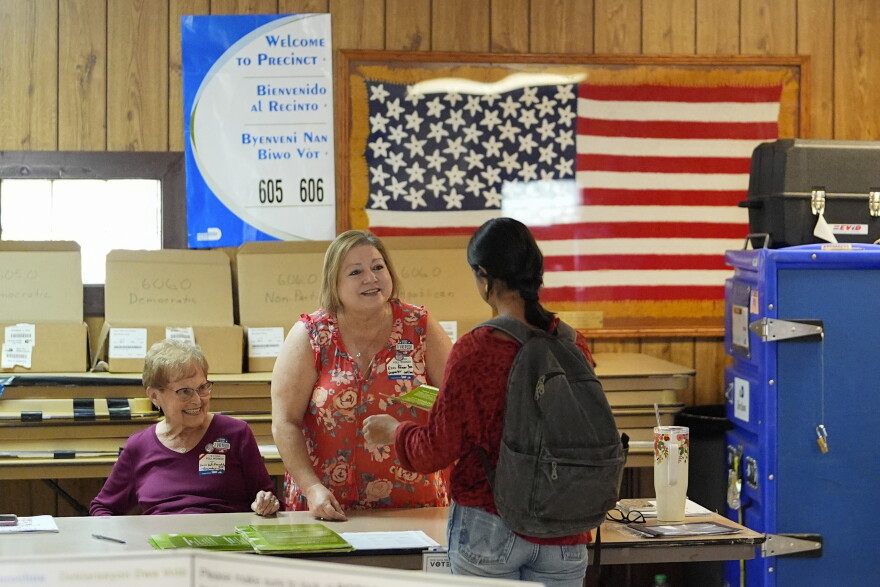 Poll worker hands a voter a ballot at a polling station inside the American Legion in South Miami, Fla.