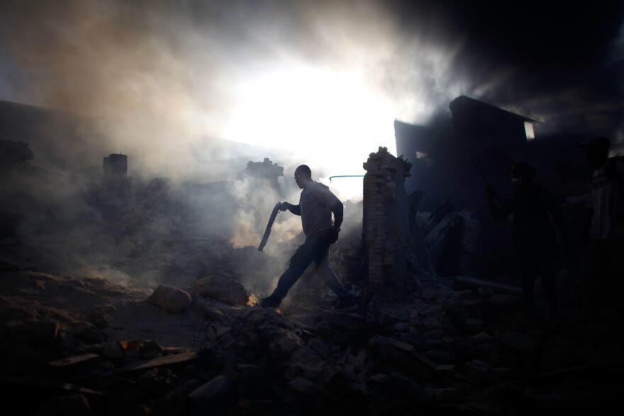 A man carries a shotgun in an attempt to keep looters at bay as he walks through a collapsed burning building in the commercial district of downtown Port-au-Prince.