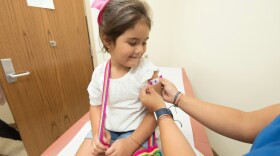A little girl in a doctor's office receives a colorful bandaid on her arm after a shot. 