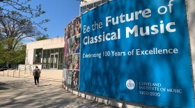 A person walks past the circular exterior of the Cleveland Institute of Music where a bright blue banner reads, "Be the future of classical music."