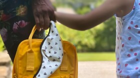 Mother and child waiting together for the school bus, holding a face mask and a backpack. (Getty Images)