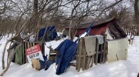 A shelter made of a tent and tarps with a wooden pallet fence.