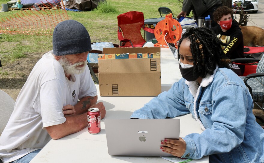  Jesse Hawkins sits outside at a table with a volunteer looking at a laptop screen. 