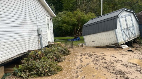 A storage shed that has been knocked over by flood waters sits in a muddy yard.