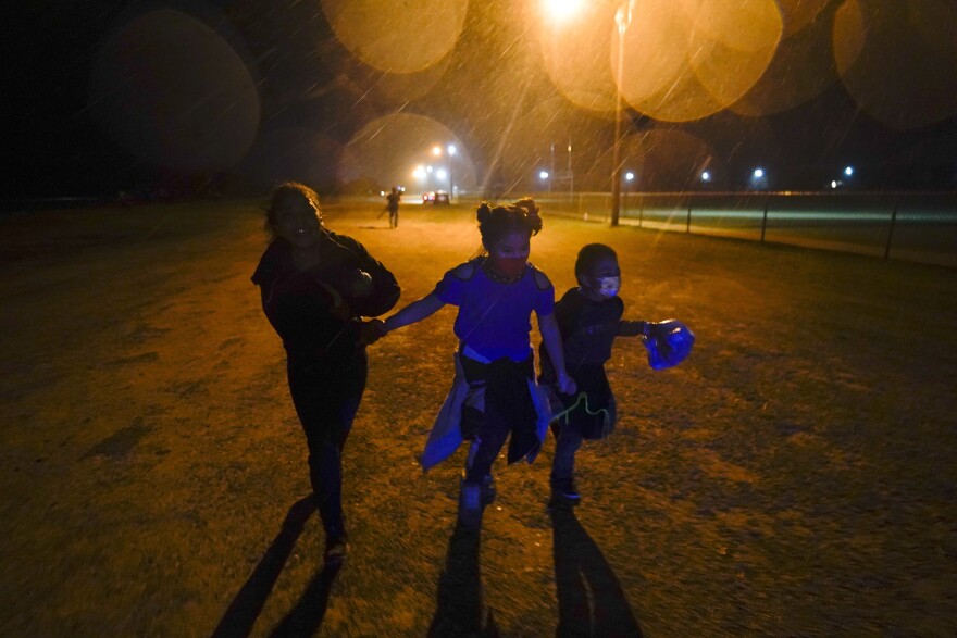 FILE - In this May 11, 2021, file photo, three young migrants hold hands as they run in the rain at an intake area after turning themselves in upon crossing the U.S.-Mexico border in Roma, Texas. Five months after the Biden administration declared an emergency and raced to set up shelters to house a record number of children crossing the U.S.-Mexico border alone, kids continue to languish at the sites, while more keep coming, child welfare advocates say. (AP Photo/Gregory Bull, File)